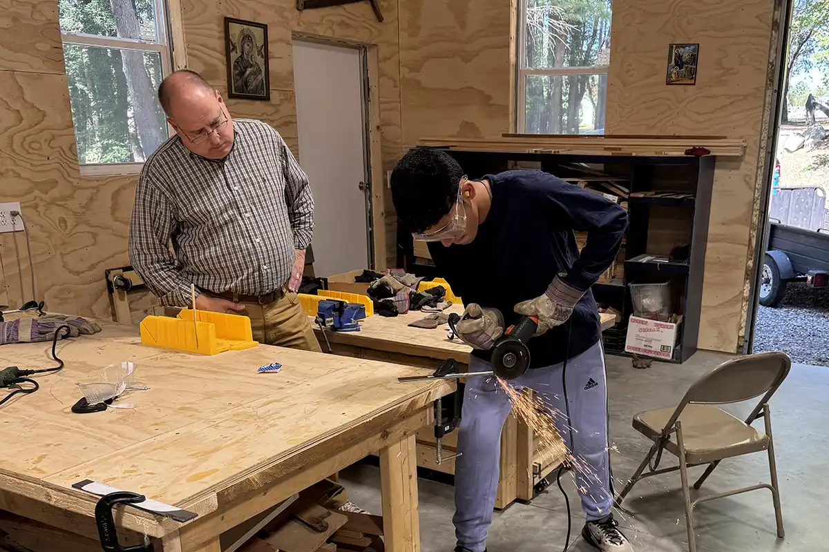 teacher-boy-student-speaking-picnic-table Craftsmanship program with teacher watching student cut metal