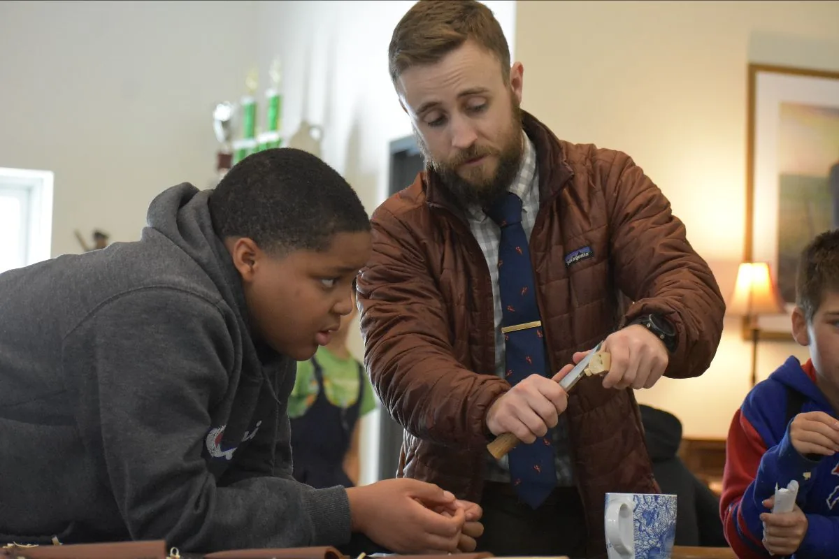 A teacher showing a middle school student proper whittling technique