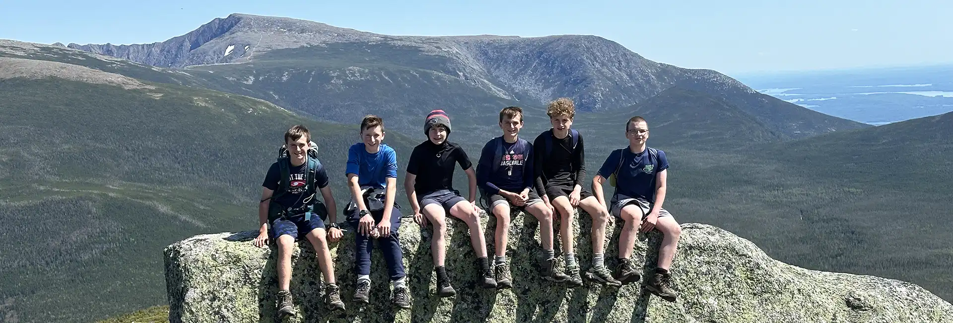 Six boys sitting on rock overlooking mountain view