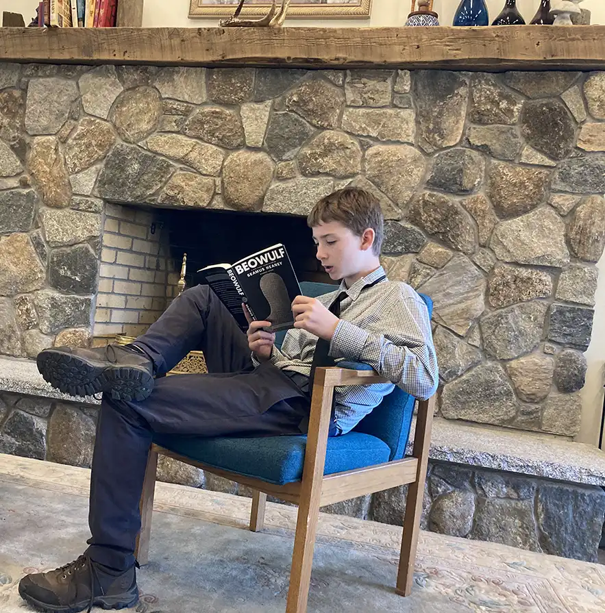 Male student sitting by fireplace reading Beowulf