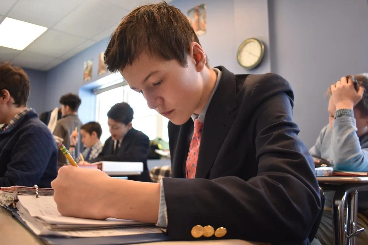 Eighth grade boy takes notes in a classroom at Sparhawk Academy